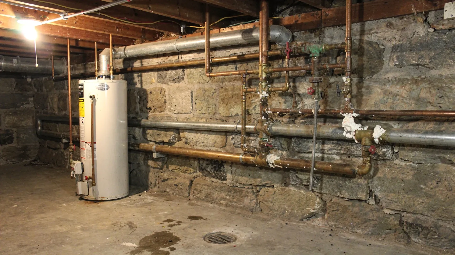 A Kingston older-home basement utility area with visible copper and some older piping, showing mineral scale around fittings and valves, plus a water heater nearby. The scene should feel like a real Kingscourt home mechanical space.