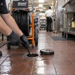 A drain specialist feeds a jetting hose into a restaurant cleanout to remove buildup from a kitchen line.